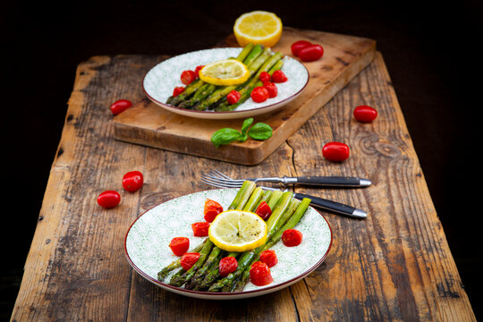 Grilled green asparagus with tomato and lemon on wooden table