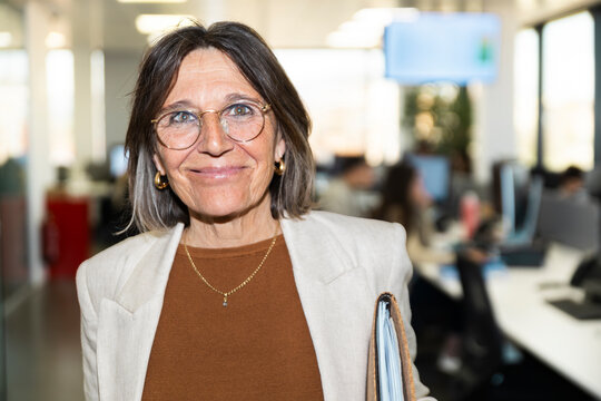 Smiling businesswoman holds a folder in a busy corporate office