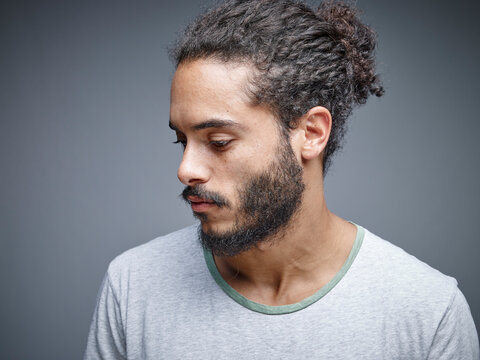 Bearded young man with curly brown hair wearing t-shirt in front of grey background