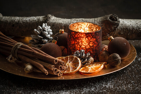 Christmas decoration with tea light candle, christmas tree balls, cinnamon sticks, slices of dried oranges and walnuts on plate, studio shot