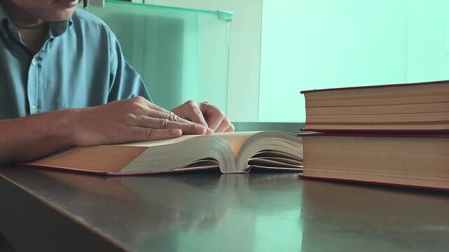 asian senior man reading a stack of books in a quiet library during daytime, focused elderly scholar studying indoors