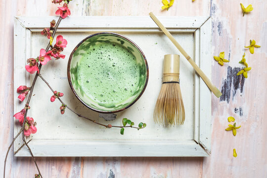 Matcha tea in bowl, with match powder, spoon and chasen and pink flowers