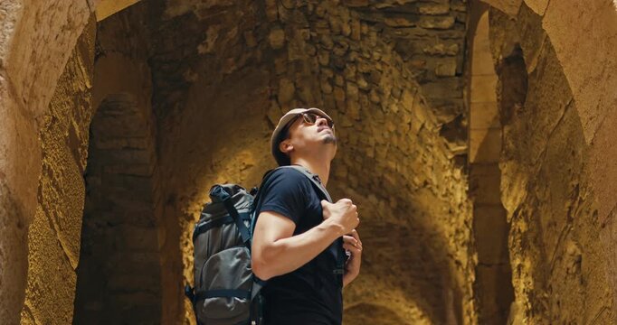 Low angle view of a male tourist with a backpack looking up while exploring the historic stone interior of Ajloun Castle, Jordan, illuminated by warm natural light in the medieval fortress