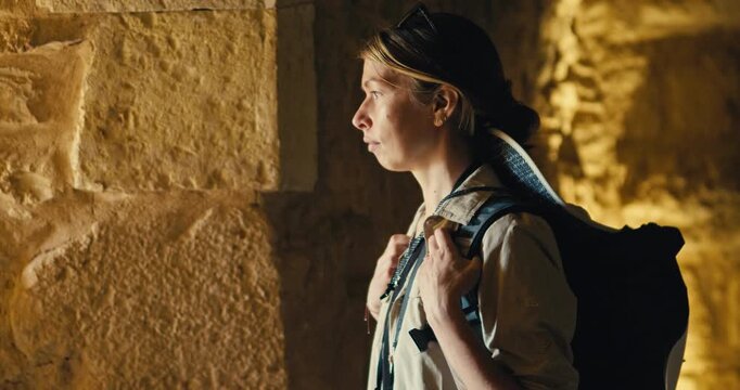 Female tourist with a backpack pauses inside Ajloun Castle, Jordan, illuminated by warm natural light while exploring the historic medieval fortress and its stone architecture