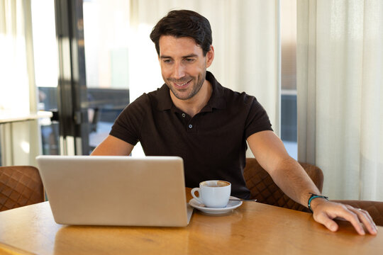 Smiling man working on laptop with coffee at cafe