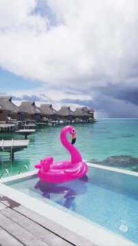 Holidays Vacation Getaway Concept. Funny vacation beach pool travel concept with inflatable pink flamingo float toy mattress in luxury swimming pool. SLOW MOTION. Raw unedited vertical video.