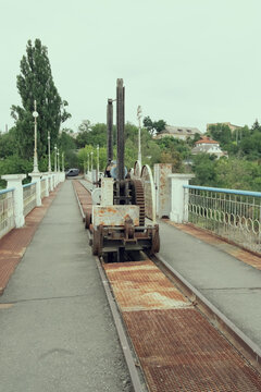 Old rusty mechanical winch mechanism on rails along concrete bridge of Korsun Shevchenkivskyi hydroelectric dam, industrial engineering equipment backdrop.