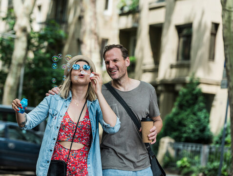 A happy couple walks in the city while the woman blows soap bubbles