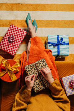 A stylish woman unwraps a colorful Christmas gift on the couch
