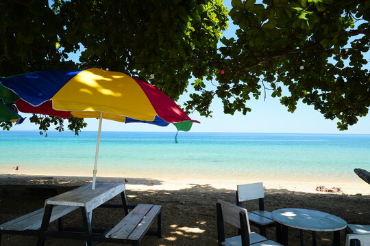 Colorful Beach Umbrella and Wooden Chairs Beside Turquoise Tropical Sea