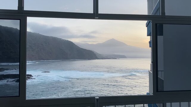 Scenic view of Mount Teide at sunset from an apartment window in Tenerife, Canary Islands, Spain. The video shows the calm, gently rolling ocean in the foreground with the silhouette of Teide mountain