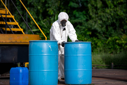 Workers in protective suits handle blue chemical barrels during hazardous material safety training