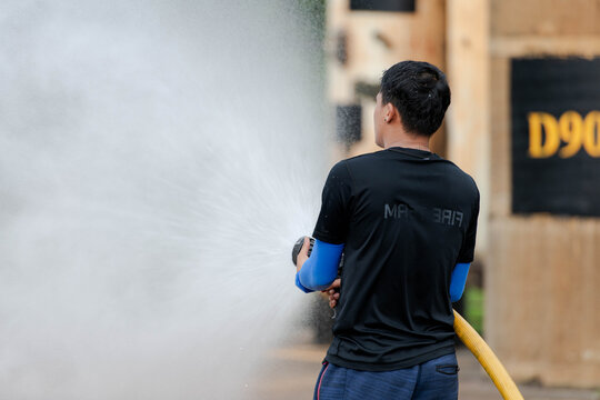 A firefighter sprays water from a yellow hose during firefighting training at an industrial facility