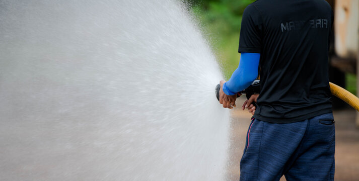 A firefighter sprays water from a yellow hose during firefighting training at an industrial facility