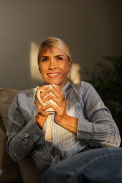 Woman Sits on a Sofa in a Home Setting, Enjoying a Warm Drink While Relaxing Without Digital Devices During the Afternoon Light