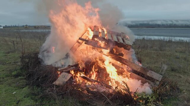A controlled burn disposes of grapevine prunings and wooden materials after seasonal vineyard work, with flames rising against a peaceful countryside backdrop.
