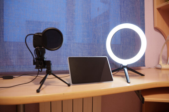 Tablet, microphone and ring light on wooden desk beside bright window, creating clean home studio setup for recording, streaming, teaching and digital, with tablet, microphone, ringlight, desk detail