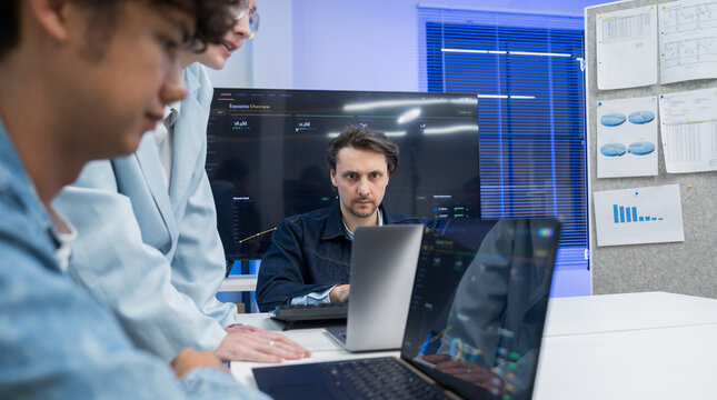Diverse group of developers standing over desk and concentrating on laptop screen during AI project review.