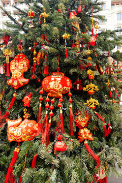 Chinese New Year tree decorated with red ornaments and tassels, showcasing traditional symbols and vibrant colors in a festive urban setting
