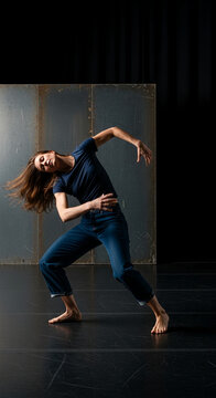 A female dancer in jeans moves expressively on a dark stage, embodying freedom, movement, and artistic performance