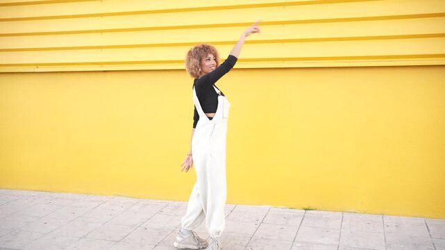 A stylish model is confidently posing in trendy white overalls against a bright yellow wall