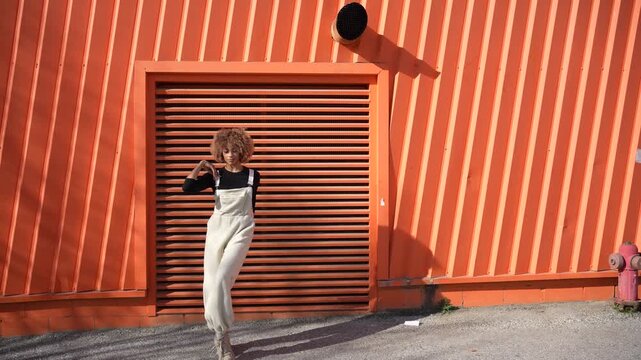 A stylish woman is strolling gracefully near a vibrant and eyecatching orange wall