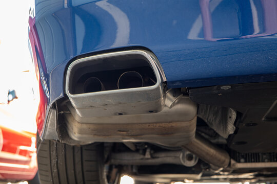 Low angle close up view showing rectangular chrome exhaust tip surround, dual tailpipes, and rear silencer box on a blue car.