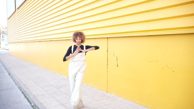 A Cheerful Woman Smiling and Posing in Front of a Bright Yellow Wall with a Fun Vibe