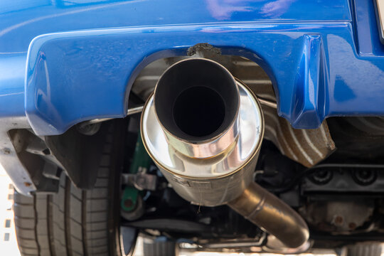 Low angle view looking into a large polished cannon exhaust tailpipe tip and rear silencer box on a raised blue vehicle.