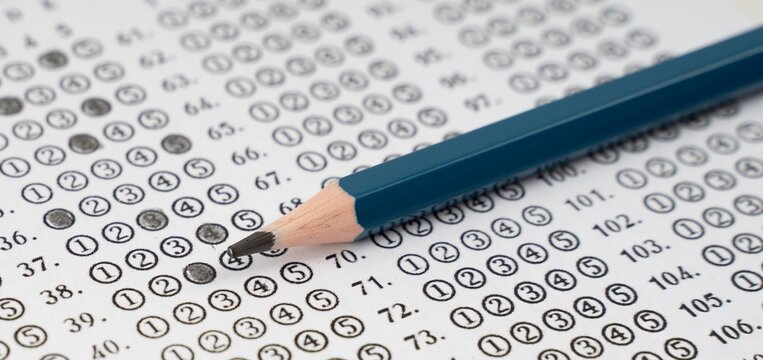 Blue pencil rests beside a test sheet. Darkened circles mark answers on exam paper. Question numbers line the page in orderly rows. Focal point emphasizes concentration and decision