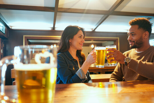 Young adult Caucasian woman and Black man clinking beer mugs in pub, socializing after work and expressing connection. Ideal for dating, nightlife, friendship, hospitality marketing