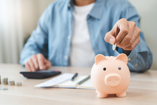 Young people saving money monthly expenses putting coin in to piggy bank on the table.