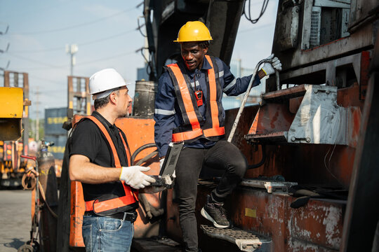 Two logistics technicians discuss heavy reach stacker maintenance plan using laptop computer at container forklift machinery at port terminal