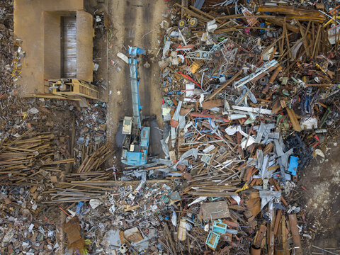 Aerial view of a blue excavator working in a scrap metal recycling yard in Agnesberg, surrounded by piles of discarded metal and industrial debris in Gothenburg, Vastra Gotaland Count, Sweden.