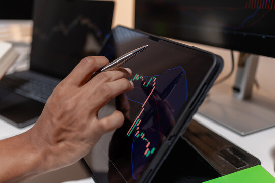 Professional trader analyzing stock market charts across multiple screens using laptop and tablet to monitor price movements, technical indicators and investment strategies in modern trading workspace