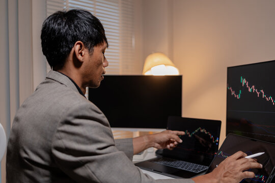 Professional trader analyzing stock market charts across multiple screens using laptop and tablet to monitor price movements, technical indicators and investment strategies in modern trading workspace