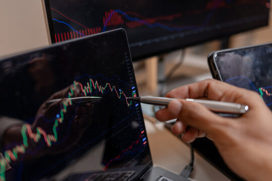 Professional trader analyzing stock market charts across multiple screens using laptop and tablet to monitor price movements, technical indicators and investment strategies in modern trading workspace