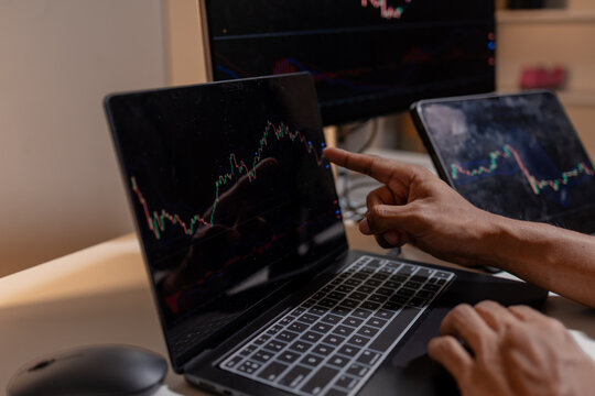 Professional trader analyzing stock market charts across multiple screens using laptop and tablet to monitor price movements, technical indicators and investment strategies in modern trading workspace