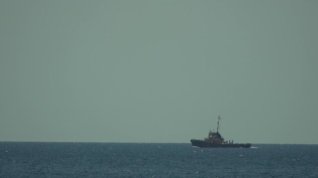 Industrial tow boat travels across vast open sea waters on a clear sunny day. Long distance wide angle shot.