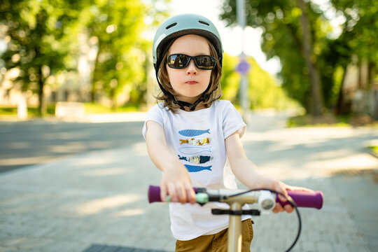 Young boy wearing a safety helmet rides a kick scooter on a city sidewalk. Active childhood, urban mobility and road safety for children.