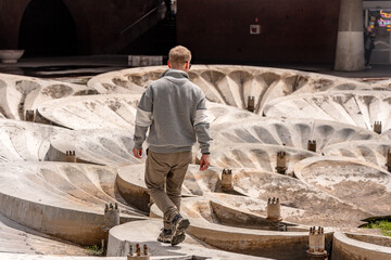A man is traveling in Armenia, near a sculptural stone fountain with overlapping bowls featuring relief patterns at the entrance to the metro station. © KseniaJoyg