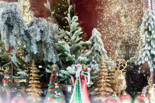Christmas window display showcases decorated evergreen trees, colorful ornaments, and a festive figurine in a snowy environment, illuminated by twinkling lights creating a holiday atmosphere
