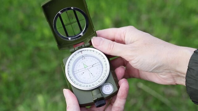 Traveler opens a compass and uses it to navigate the outdoors during a summer hike. Concept of travel