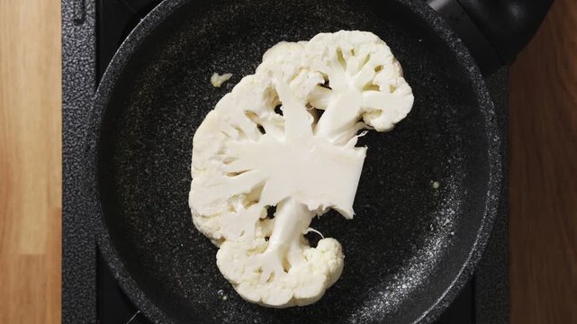 Cauliflower is placed in frying pan for cooking. Cauliflower curry blends coconut milk, chickpeas, onion, garlic and spices. Serve cauliflower curry with rice, naan, yoghurt, coriander or lime.