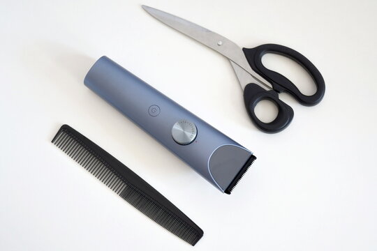 Flat lay composition of hair grooming essentials featuring a cordless electric trimmer, black hair comb, and stainless steel scissors neatly arranged on a clean white background.