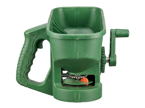 Handheld lawn seed fertilizer spreader green plastic manual hand crank tool for garden care lawn maintenance isolated on black background for agriculture farming landscaping work product cutout.
