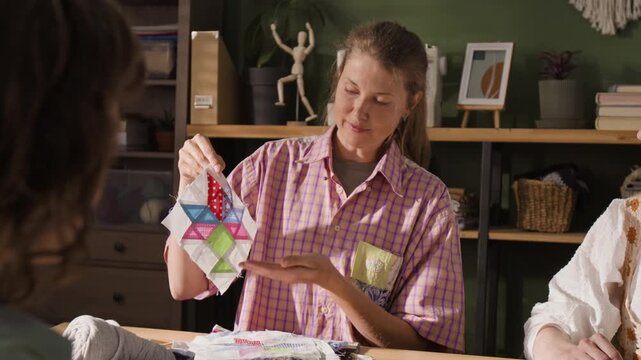 Caucasian woman showing handmade patchwork quilt block to students during creative craft workshop. Clip is ideal for promoting community education, DIY hobbies, and sewing classes