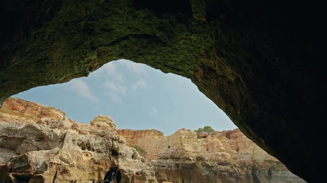 Sunlit limestone cliffs framed by the dark interior of Devils Eyes Cave on the Algarve coast.