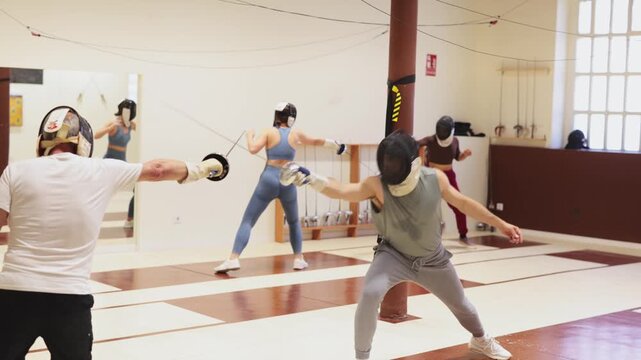 Group of fencers trains in duels and works out blows on the pillows in the gym