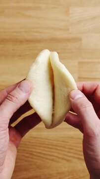 Hands open hot bao bun just after steaming. Hot bao bun releases heat from soft centre, showing fresh steamed bread. Enjoy hot bao bun immediately with chilli sauce, soy dip or soup.